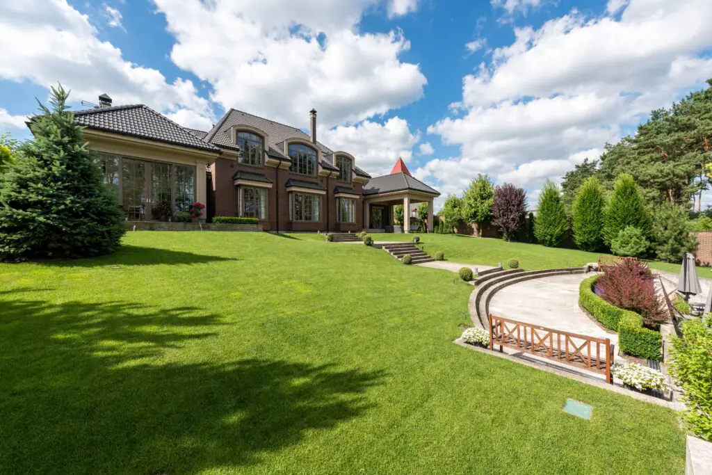Elegant brick mansion with manicured lawn and garden under a bright blue sky.