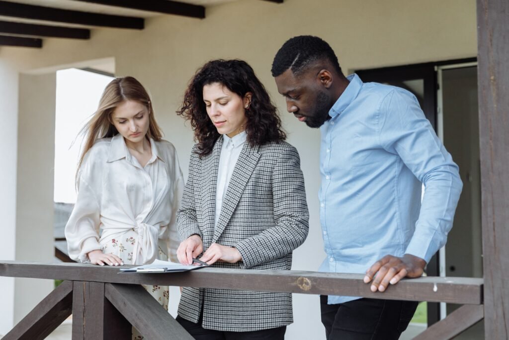 Common Mistakes Property Buyers Make in Abuja (And How to Avoid Them) Three adults reviewing documents on a balcony during a real estate consultation.